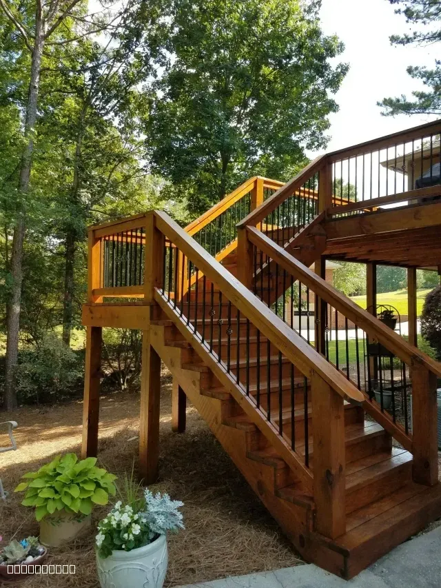 Newly stained wooden deck stairs with black metal railings and a warm honey finish.