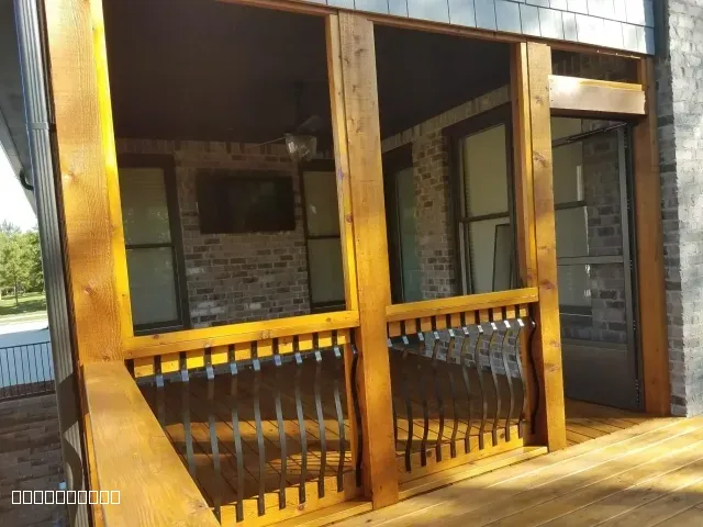 A professionally stained wooden screened-in porch with black metal railings and a brick wall background.