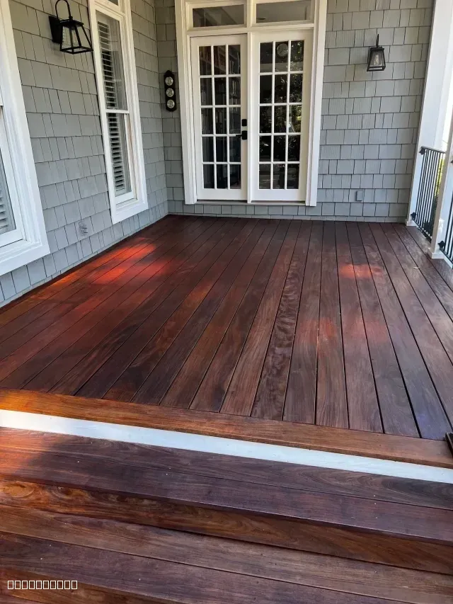 A freshly stained dark wood deck with a rich reddish-brown finish next to a house with grey siding.