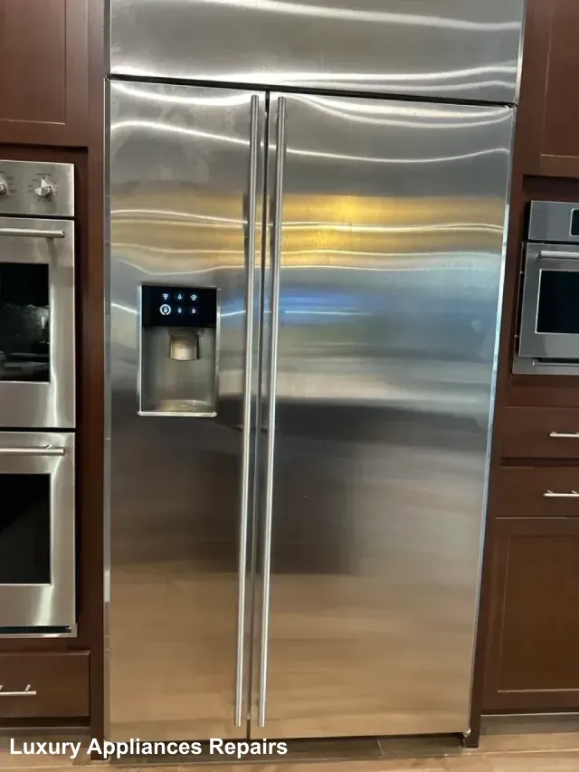 A large built-in stainless steel side-by-side refrigerator integrated into dark wood kitchen cabinets.