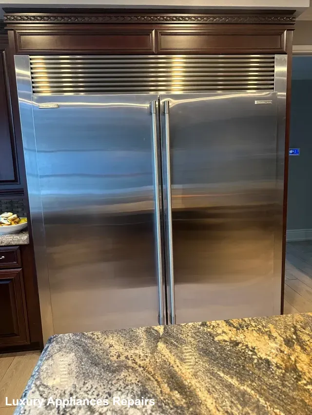 A built-in stainless steel refrigerator integrated into dark wood kitchen cabinets.