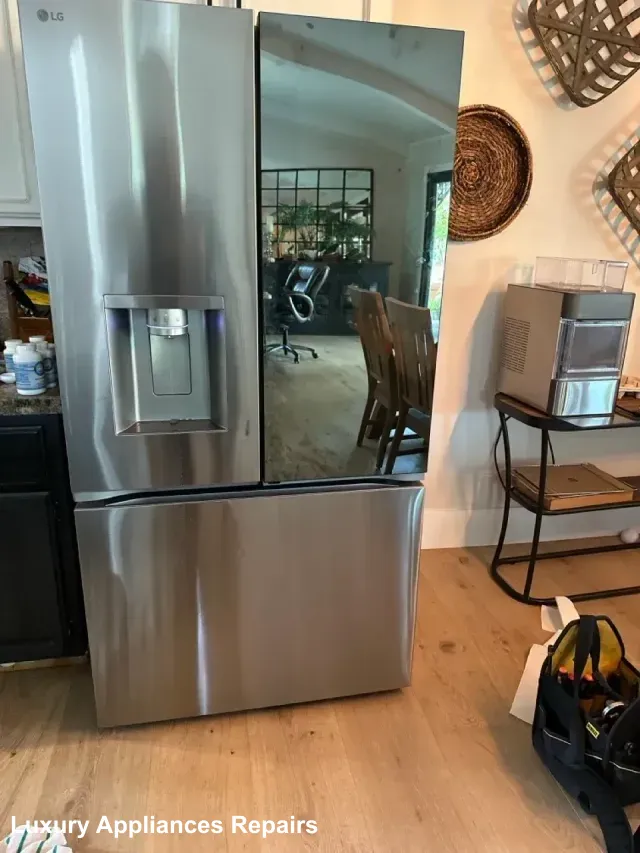 A stainless steel LG French door refrigerator with a glass door panel and water dispenser being serviced.