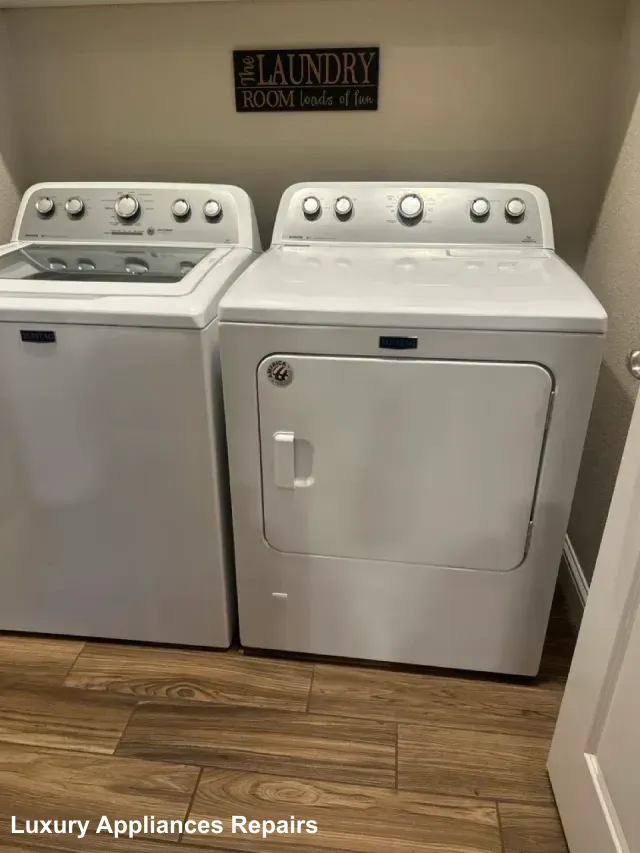 A white top-load washer and front-load dryer set in a laundry room with wood floors.