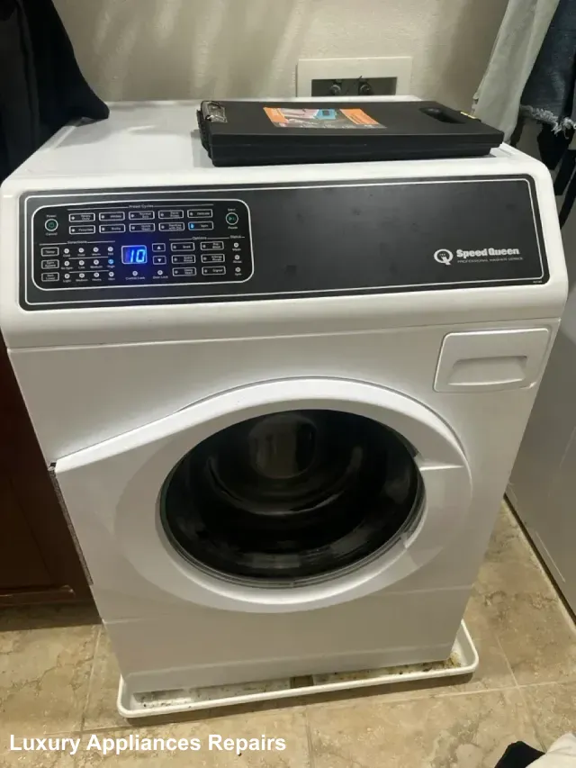 A white Speed Queen front-load washing machine with an active digital display during a repair service.