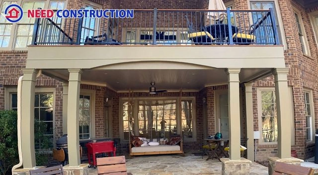 A two-story outdoor living area featuring an upper deck with black railings and a finished underdeck patio with a ceiling fan and daybed.