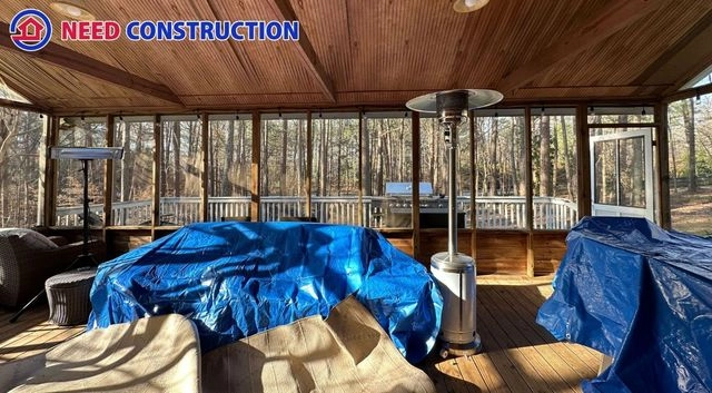 A large screened-in porch with a wood ceiling and floor overlooking a wooded backyard.