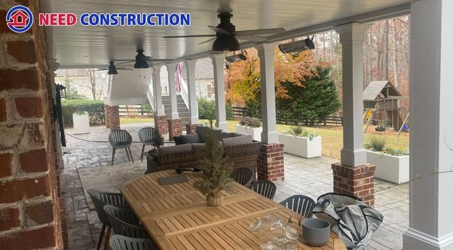 A luxurious covered patio featuring a wooden dining table, ceiling fans, and brick-based columns by Need Construction.