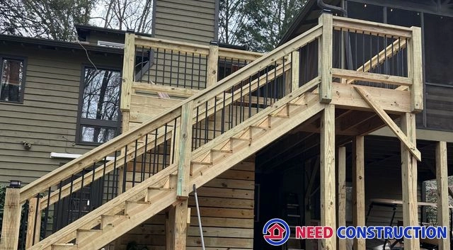 A newly built wooden deck with a staircase featuring black metal railings attached to a house.