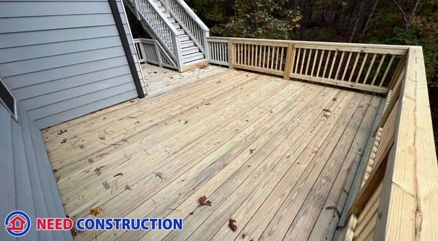 A newly installed wooden deck with railings attached to a house with grey siding.