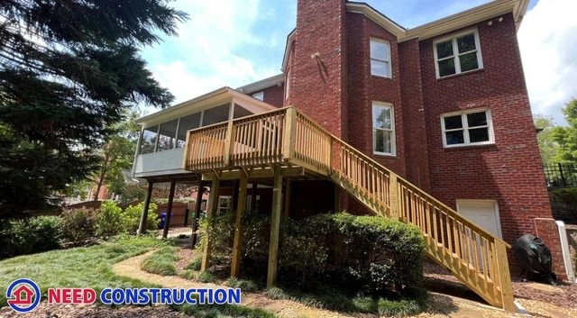 A large red brick house featuring a new wooden deck with stairs and an elevated sunroom addition.