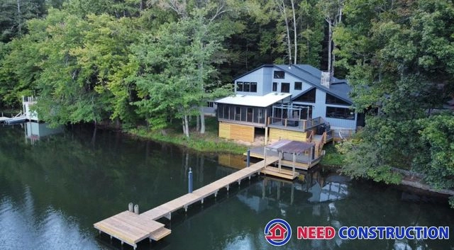 Aerial view of a modern grey lakefront house with a large wooden deck and a long dock extending into the water.
