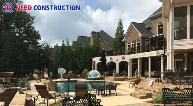 A luxurious backyard featuring a custom swimming pool, stone patio, and multi-level deck by Need Construction.