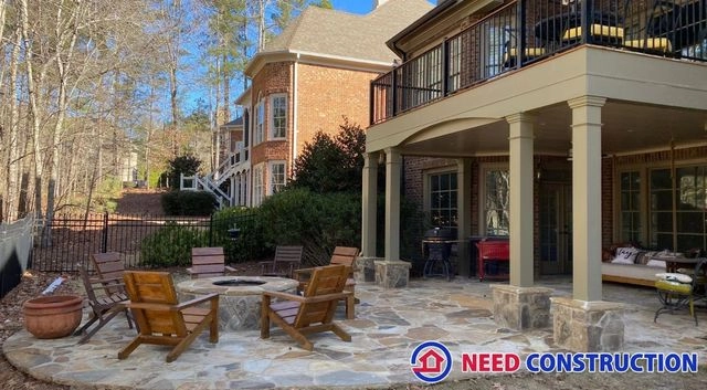 A luxurious backyard outdoor living space featuring a stone patio with a fire pit and a covered underdeck patio area.