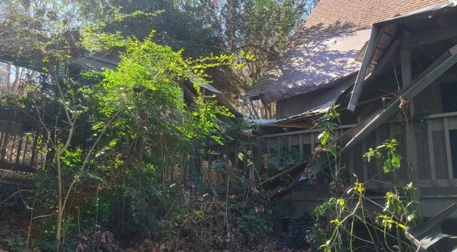 Severe structural damage to a house roof and porch with collapsed beams and debris.