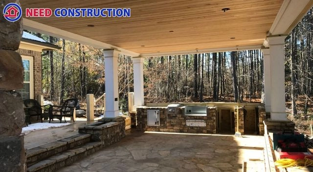 A luxurious custom outdoor kitchen and stone patio under a wood-paneled porch ceiling.