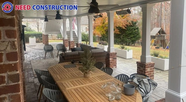 A luxurious covered patio with a wooden dining table, lounge furniture, and ceiling fans under a white finished ceiling.