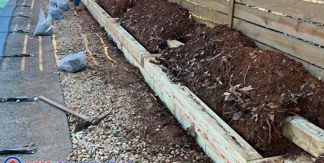 Construction of a wooden timber retaining wall for an outdoor living space near a pool.