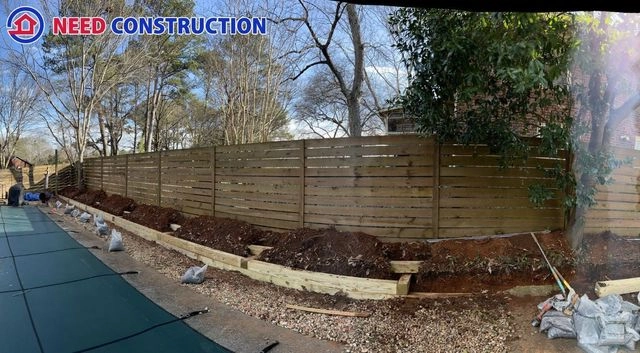 A horizontal wood privacy fence and timber retaining wall being installed in a backyard next to a pool.