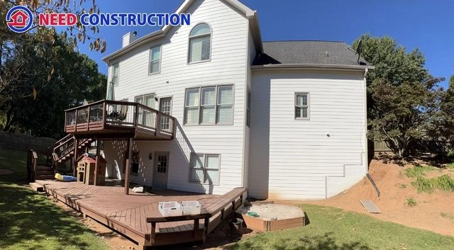 A large white house with a multi-level wooden deck and white siding by Need Construction.