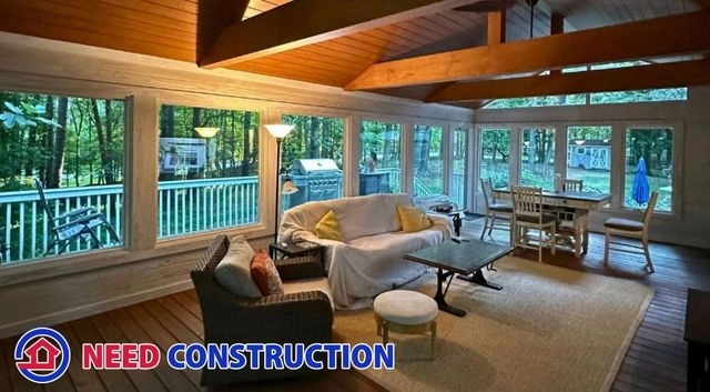 Interior view of a luxury sunroom with vaulted wood ceilings and large windows overlooking a forest.