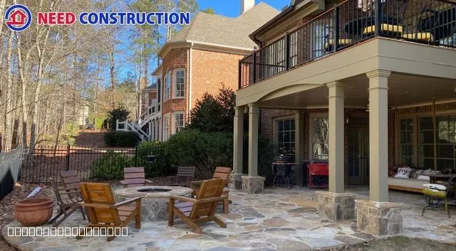 A luxurious stone patio with a fire pit and wooden chairs under a covered deck at a brick home.