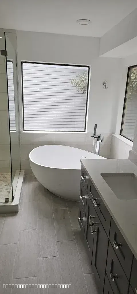 Completed bathroom remodel featuring a freestanding tub, glass shower, and gray vanity with quartz countertop.