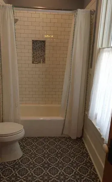 A renovated bathroom featuring white subway tiles on the shower wall, a mosaic niche, and patterned floor tiles.