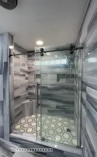 Modern walk-in shower with grey marble wall tiles, hexagon floor tiles, and a sliding glass door.