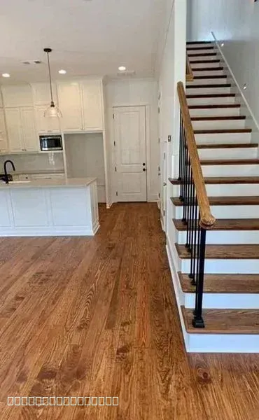 Modern home interior featuring white kitchen cabinets and newly installed hardwood flooring next to a wooden staircase.