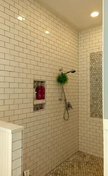 A newly remodeled shower with white subway tiles, a recessed niche, and hexagonal mosaic floor tiles.