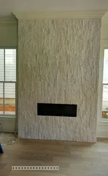 A modern floor-to-ceiling fireplace with light grey stacked stone tile and a recessed black linear fireplace unit.