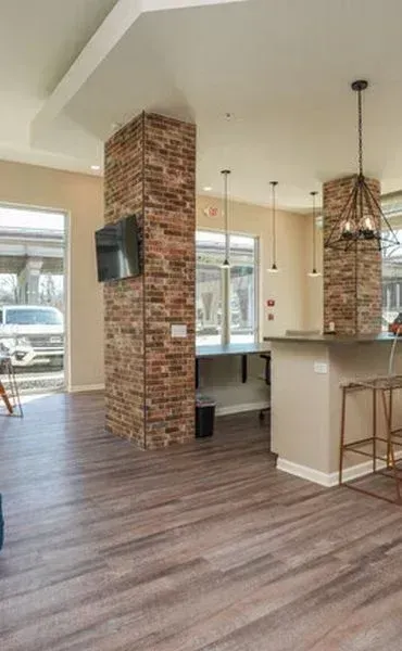 Modern interior room featuring wood-look flooring, brick-wrapped columns, and a kitchen island with industrial lighting.