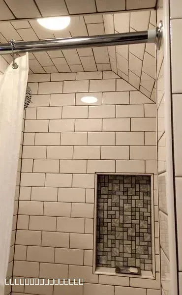 A modern bathroom shower featuring white subway tiles, dark grout, and a decorative mosaic recessed niche.