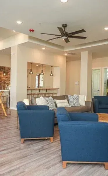 Modern open-concept living room with blue chairs, wood-look floors, and a kitchen bar area.