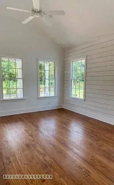A bright room with polished hardwood floors, white shiplap walls, and large windows.