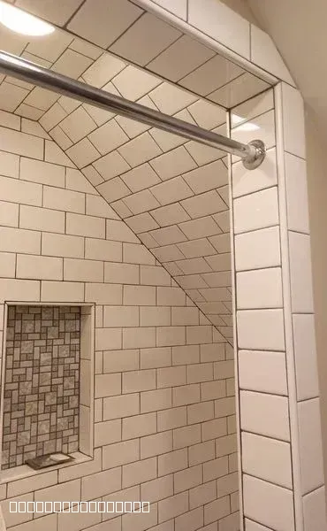 White subway tile installation in a shower with a sloped ceiling and a recessed mosaic tile niche.