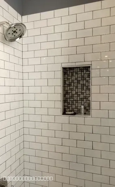 White subway tile shower walls with a decorative mosaic recessed niche and chrome shower head.