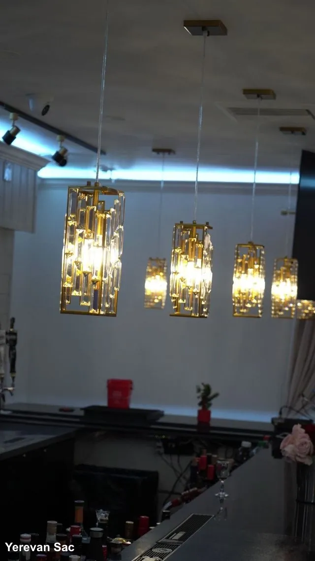 A series of luxurious rectangular crystal pendant lights with gold frames hang above a dark bar counter — Yerevan Sac, Carmichael CA