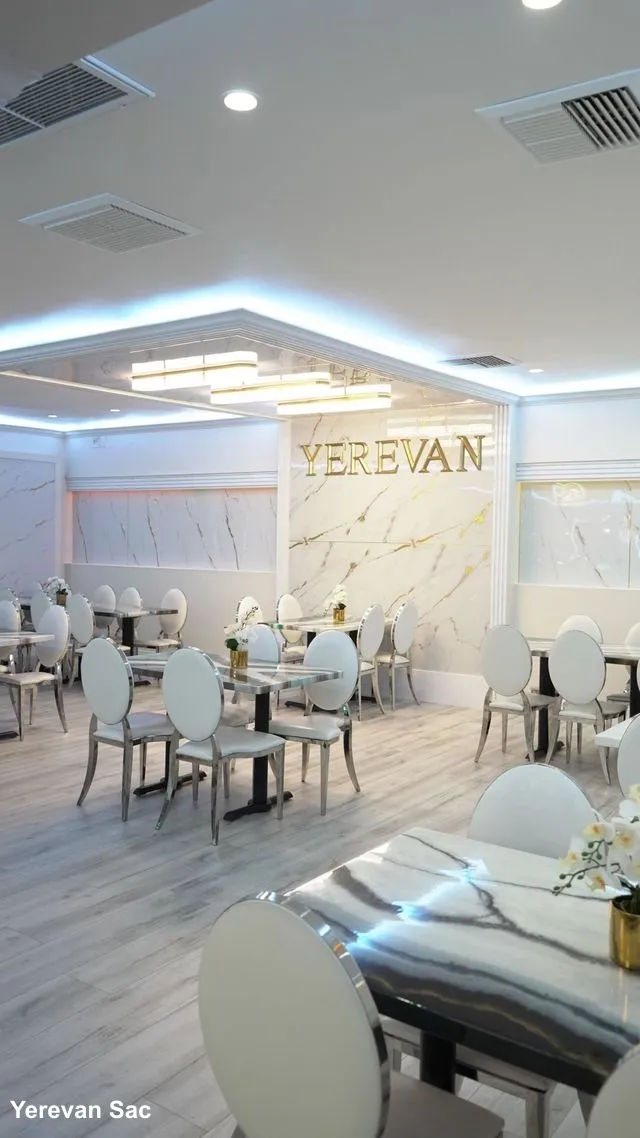 A bright and modern restaurant dining area featuring white marble-topped tables, stylish white chairs with metallic frames, and light wood flooring — Yerevan Sac, Carmichael CA